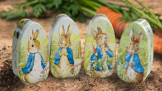 Decorative tin containers with Peter Rabbit illustrations, displayed on a rustic surface with carrots